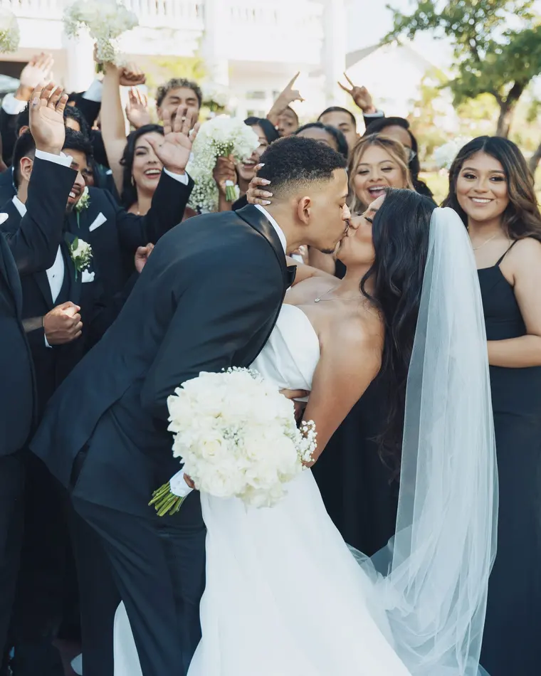 A kiss, surrounded by the wedding party